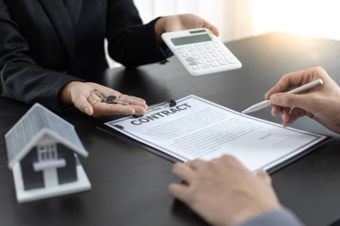 Emlakçı müşteriye gönderilecek anahtarları elinde tutuyor ve ev satışı anlaşmasını ve ev sigortasını müşteriye, ev satışları ve ev sigortası kavramına imzalama şartlarını sunuyor..