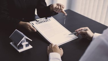 Emlakçı müşteriye gönderilecek anahtarları elinde tutuyor ve ev satışı anlaşmasını ve ev sigortasını müşteriye, ev satışları ve ev sigortası kavramına imzalama şartlarını sunuyor..