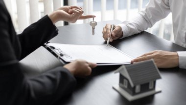 Emlakçı müşteriye gönderilecek anahtarları elinde tutuyor ve ev satışı anlaşmasını ve ev sigortasını müşteriye, ev satışları ve ev sigortası kavramına imzalama şartlarını sunuyor..