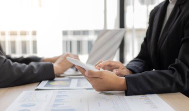 Şirketin gelir grafiğiyle ilgili iş adamları, yöneticiler ve muhasebecilerden oluşan bir ekiple ofiste dizüstü bilgisayarlar, hesap makineleri ve finans konseptiyle bir araya gelmek.