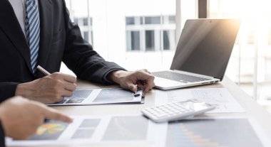 Şirketin gelir grafiğiyle ilgili iş adamları, yöneticiler ve muhasebecilerden oluşan bir ekiple ofiste dizüstü bilgisayarlar, hesap makineleri ve finans konseptiyle bir araya gelmek.