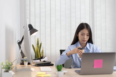 Asyalı kadınlar dizüstü bilgisayarlardaki finansal verileri analiz ediyor ve odada kahvelerini yudumluyor..