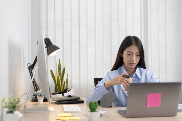 Asian women are analyzing financial data on laptops and sipping coffee at the room, Working alone in the home office concept.