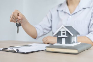 Emlakçı müşteriye gönderilecek anahtarları elinde tutuyor ve ev satışı anlaşmasını ve ev sigortasını müşteriye, ev satışları ve ev sigortası kavramına imzalama şartlarını sunuyor..