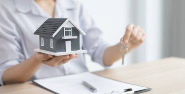 Emlakçı müşteriye gönderilecek anahtarları elinde tutuyor ve ev satışı anlaşmasını ve ev sigortasını müşteriye, ev satışları ve ev sigortası kavramına imzalama şartlarını sunuyor..