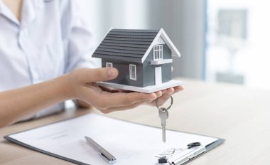 Emlakçı müşteriye gönderilecek anahtarları elinde tutuyor ve ev satışı anlaşmasını ve ev sigortasını müşteriye, ev satışları ve ev sigortası kavramına imzalama şartlarını sunuyor..