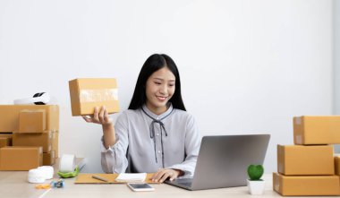 Genç Asyalı bir kadın dizüstü bilgisayarında müşteriyle sohbet ediyor ve siparişi onaylamak, ürünleri İnternet 'te satmak veya ev konseptinde serbest iş yapmak için ürünü dağıtıyor..