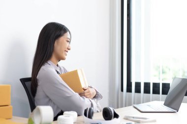 Genç Asyalı bir kadın dizüstü bilgisayarında müşteriyle sohbet ediyor ve siparişi onaylamak, ürünleri İnternet 'te satmak veya ev konseptinde serbest iş yapmak için ürünü dağıtıyor..