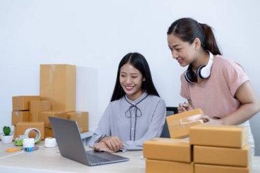 İki genç Asyalı kadın internet üzerinden alışveriş yapan müşterilere gülümseyerek sohbet ediyor ve anlaşmanın imzalanma emrini onaylıyorlar. İnternetten ürün satmak ya da ev konseptinde serbest iş yapmak..