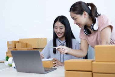 İki genç Asyalı kadın internet üzerinden alışveriş yapan müşterilere gülümseyerek sohbet ediyor ve anlaşmanın imzalanma emrini onaylıyorlar. İnternetten ürün satmak ya da ev konseptinde serbest iş yapmak..