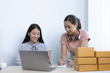 İki genç Asyalı kadın internet üzerinden alışveriş yapan müşterilere gülümseyerek sohbet ediyor ve anlaşmanın imzalanma emrini onaylıyorlar. İnternetten ürün satmak ya da ev konseptinde serbest iş yapmak..