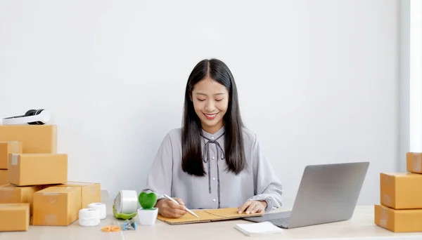 Asian businesswoman is taking online orders from a phone and chatting with customers to confirm their order, Selling products online or doing freelance work at home concept.