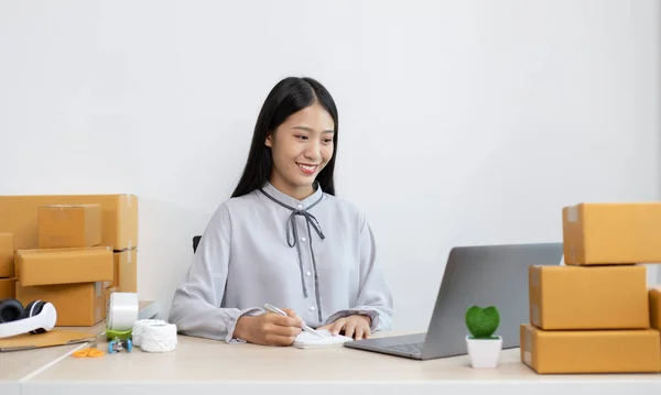 Asian businesswoman is taking online orders from a laptop and chatting with customers to confirm their order, Selling products online or doing freelance work at home concept.