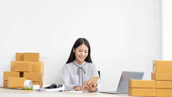 Young Asian women are selling products online and are using mobile phones to chat with customers to confirm orders, Selling products online or doing freelance work at home concept.