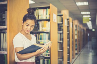 Asyalı kız öğrenciler kütüphanede okuyor ve okuyor, kütüphanede öğreniyorlar.