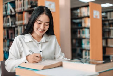 Asyalı kız öğrenciler kütüphanede okuyor ve okuyor, kütüphanede öğreniyorlar.