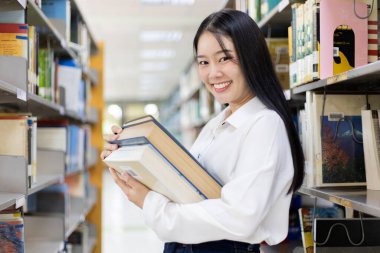 Asyalı kız öğrenciler kütüphanede okuyor ve okuyor, kütüphanede öğreniyorlar.