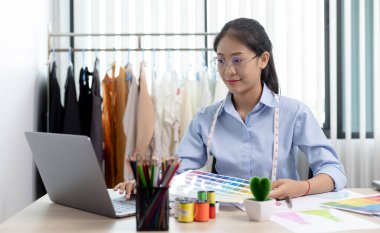 Moda tasarımcıları çalışma odalarında dizüstü bilgisayarlar ve masalarında tasarım çizimleri ile çalışıyorlar, yeni bir kıyafet koleksiyonu yaratıyorlar, tasarımcının çalışmalarının yaratımı.