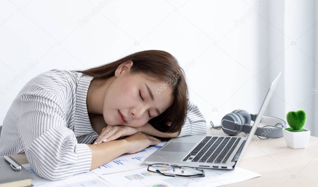 Financial accountant works on analyzing and summarizing the company's incomes and expenses in real estate and account management, causing her to get tired and fall asleep on her desk, Hard work and overtime work concept.