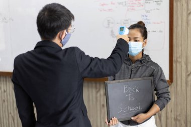 Öğretmen yüksek ateşi olan birinin vücut ısısını ölçmek ve yeni grip salgınının yayılmasını önlemek için öğrenci ya da üniversite öğrencisinin vücut ısısını ölçüyor..
