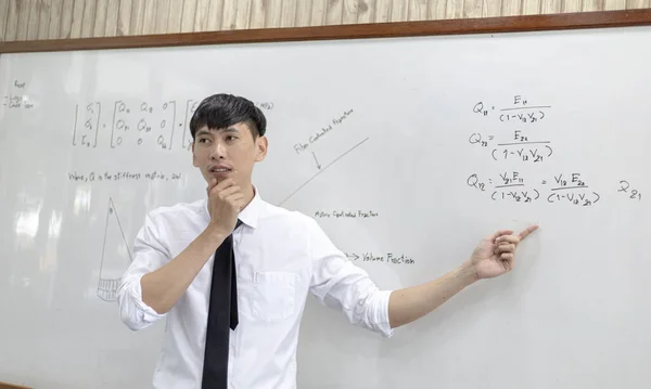 Teacher is teaching physics to students during the new school days after a long break, High school student classroom, Teacher is writing the instructional formula and explains how to do the exercises.