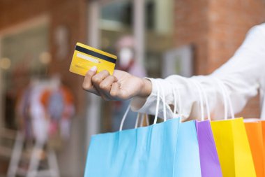Genç kadınlar renkli alışveriş yapıyorlar ve kredi kartlarını alışveriş merkezinden alışveriş yapmak için kullanıyorlar. Ürün almaktan mutlu Asyalıların tüketiciliği..