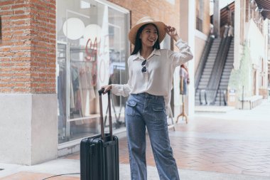 Asyalı kadın bir bavul taşıyor ve uzun hafta sonu seyahatine hazırlanmak için büyük bir şapka takıyor, Trolley çantası, uzun haftasonu seyahati, geziyi seviyorum, turizm festivali konseptini seviyorum..