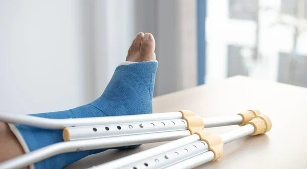 Blue ankle and foot splint Bandages on the legs from a young man\'s fall accident, Blue plaster on the ankle, Crutches assist in the walking of the patient.