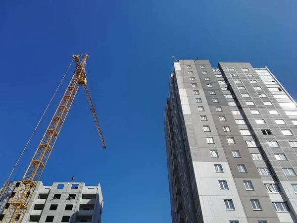 Construction crane rises above two buildings. Bottom up view on