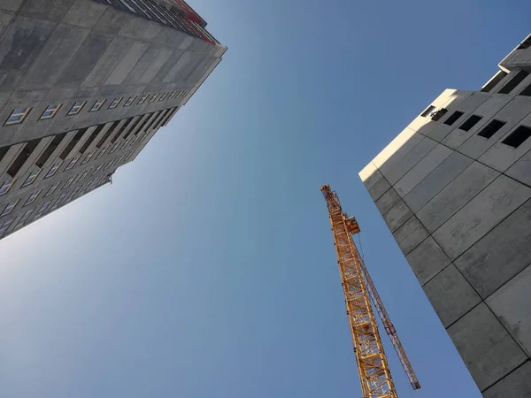 Construction crane rises above two buildings. Bottom up view on