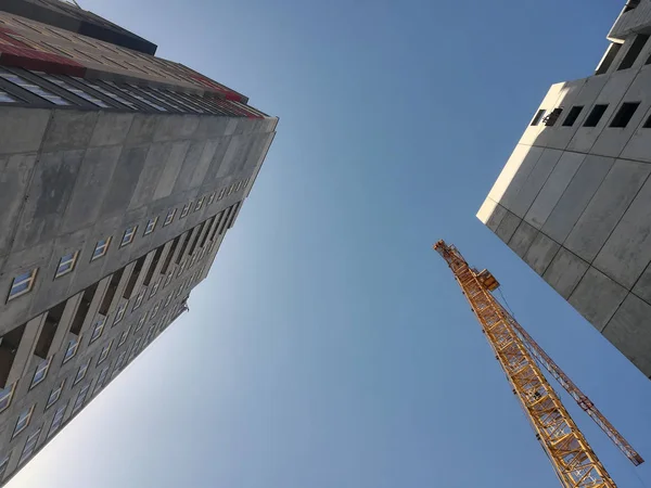 Construction crane rises above two buildings. Bottom up view on