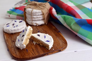 arjantinli alfajores dulce de leche ile dolu ve beyaz bir beze ile kaplanmış, ahşap bir doğrama tahtası üzerinde kurutulmuş çiçekler cornflower ile süslenmiş, beyaz bir rustik masa üzerinde