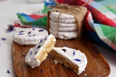 arjantinli alfajores dulce de leche ile dolu ve beyaz bir beze ile kaplanmış, ahşap bir doğrama tahtası üzerinde kurutulmuş çiçekler cornflower ile süslenmiş, beyaz bir rustik masa üzerinde