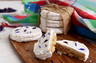 arjantinli alfajores dulce de leche ile dolu ve beyaz bir beze ile kaplanmış, ahşap bir doğrama tahtası üzerinde kurutulmuş çiçekler cornflower ile süslenmiş, beyaz bir rustik masa üzerinde