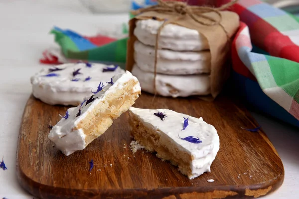 arjantinli alfajores dulce de leche ile dolu ve beyaz bir beze ile kaplanmış, ahşap bir doğrama tahtası üzerinde kurutulmuş çiçekler cornflower ile süslenmiş, beyaz bir rustik masa üzerinde