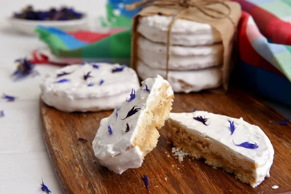 arjantinli alfajores dulce de leche ile dolu ve beyaz bir beze ile kaplanmış, ahşap bir doğrama tahtası üzerinde kurutulmuş çiçekler cornflower ile süslenmiş, beyaz bir rustik masa üzerinde
