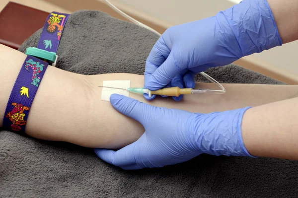 A nurse at the clinic introduces a catheter into a vein for a patients blood test. Hands of a medical worker in blue gloves, takes blood for analysis from a patient.