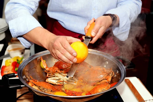 The process of making whole crabs in a wok pan, close up. Grilled crabs. The cook is cooking red crabs with vegetables. The cook rubs the zest of the orange in the process of cooking crabs.