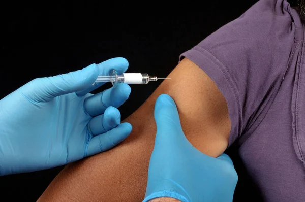 黒い背景に大きな腕にワクチンを注入する — ストック写真