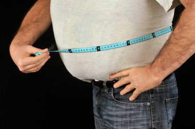 Koca göbeğini siyah arka planda yakından ölçen bir adam.