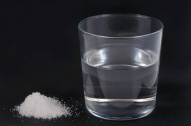 Siyah arka planda bir bardak su ve bikarbonat.