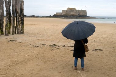 Sillon sahilinde şemsiyeli bir kadın Saint-Malo 'da Forrt National' a bakıyor. 