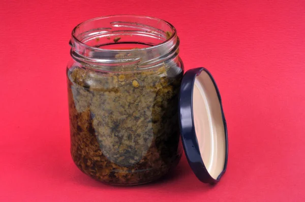 Kırmızı Arkaplanda Bir Kavanoz Pesto Sosu Açıldı — Stok fotoğraf