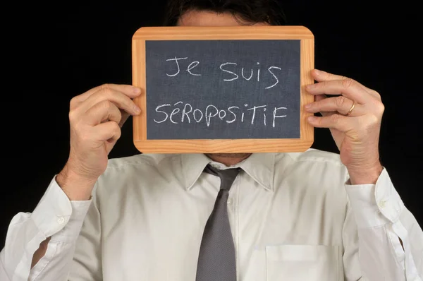 一个匿名的男人用一块写着我的法语血清呈阳性的学校写字板掩着他的脸 — 图库照片
