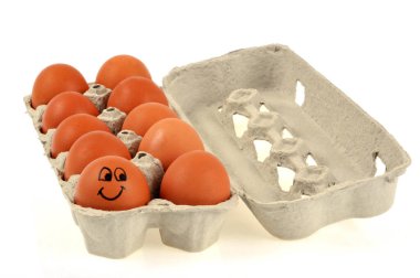 Kabuğuna gülen surat çizilmiş yumurta, beyaz bir arka planda yumurta kutusuna yakın plan. 