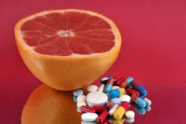 Half grapefruit with assorted drugs on red background