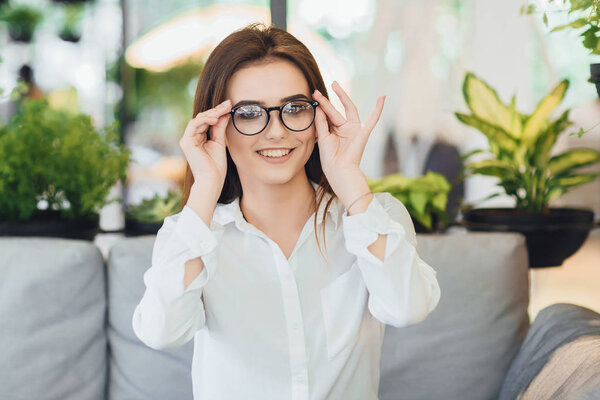 Молодая деловая женщина в очках в белой рубашке сидит в офисе
