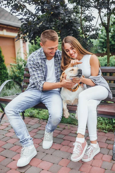 Lächelndes Paar Sitzt Mit Hund Auf Bank Park Und Konzentriert — Stockfoto