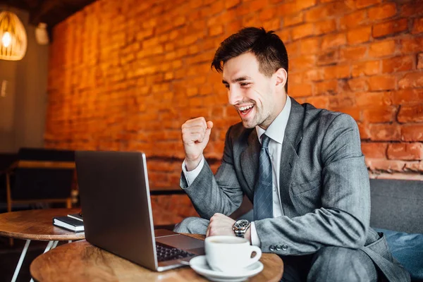 businessman looking into laptop and celebrating success project at cafe