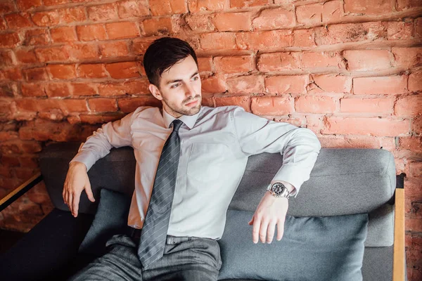 Attractive man in suit sitting at sofa at background of wall